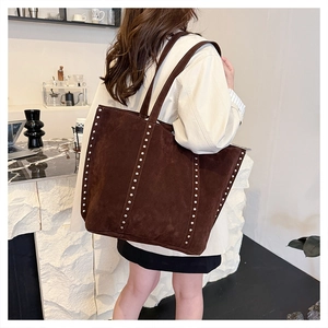 Detail view of a large brown suede tote bag featuring silver rivet studs and slim straps