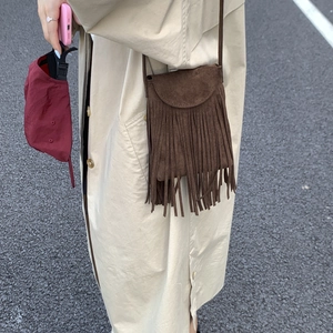 Close-up of brown suede crossbody bag with long fringes shown on a beige coat