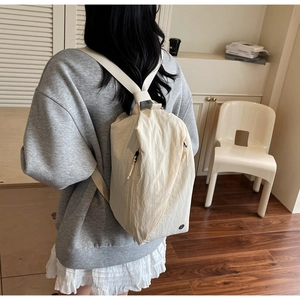 Detail of off-white nylon backpack showing the side hidden zipper and wide strap on a model