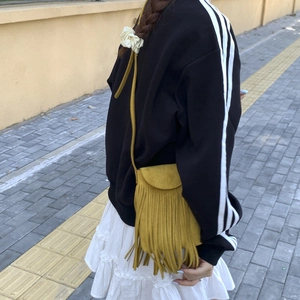 Outdoor shot showing a ginger yellow suede crossbody bag with long fringes and flap cover