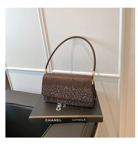 Detail of dark brown faux snake skin texture on shoulder bag with gold metal hardware