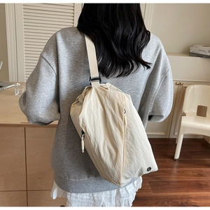 Close-up of a cream canvas crossbody bag shown on a model in a cozy home setting