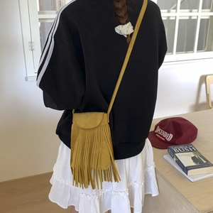 Detail of yellow matte crossbody bag with fringes worn by a model in casual setting