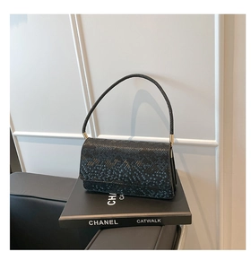 Detail view of black snakeskin embossed crossbody bag on a decorative book
