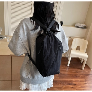 Detail of a minimalist black teardrop backpack with water-resistant fabric on a female model