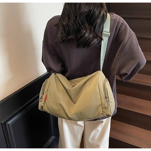 Detail view of khaki mustard nylon duffel bag with wide shoulder strap on indoor stairs