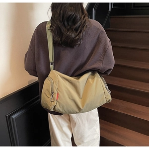 Detail of a large khaki nylon crossbody bag with wide adjustable shoulder strap on a model
