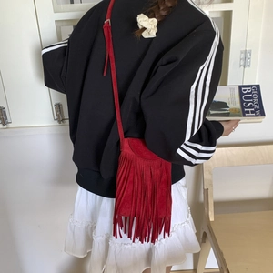 Detail view of a red suede crossbody bag with long fringes shown on a female model