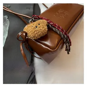 Close-up of brown leather bag with debossed logo and cute plush bear charm detail