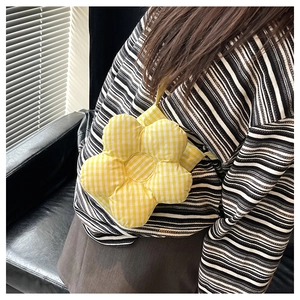 Détail du sac à bandoulière fleur à carreaux jaunes porté par un mannequin sur des rayures