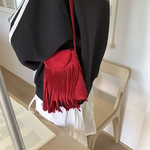 Detail of red faux suede crossbody bag with long fringes shown on a model
