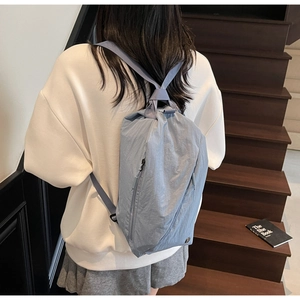 Detailed back view of a light blue nylon drawstring backpack worn by a model on stairs