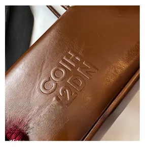 Detail of brown leather baguette bag showing pebble grain texture and embossed lettering