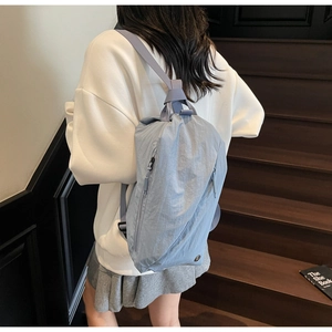 Detail of light blue nylon backpack showing side zipper and soft crinkled texture