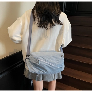 Model wearing a light blue messenger bag with crinkle texture on indoor stairs