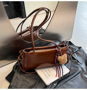 Detail view of brown leather baguette bag with embossed letters and plush bear pendant
