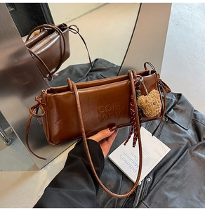 Detail of brown faux leather shoulder bag with embossed letters and a bear keychain