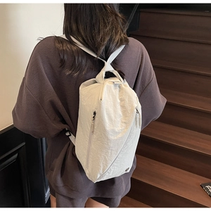 Detailed back view of a beige nylon backpack with double zipper pockets on a staircase
