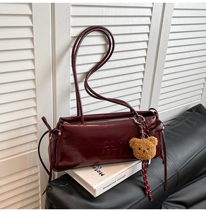 Detail of dark red patent leather shoulder bag with embossed logo and teddy bear charm