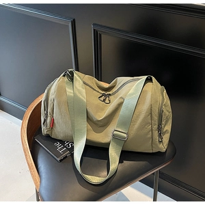 Detail of olive green nylon travel bag with adjustable strap on a black wooden chair