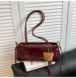 Close-up of wine red faux leather shoulder bag with bear pendant on white book