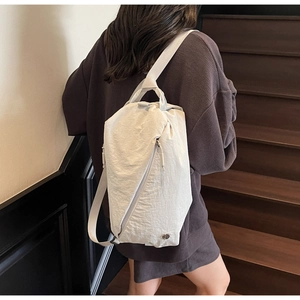 Detail of cream nylon backpack with pleated texture and side zipper on a model
