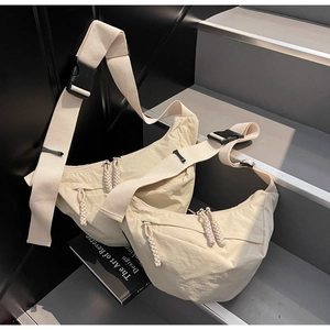 Detail view of two beige nylon crescent crossbody bags on a grey staircase setting