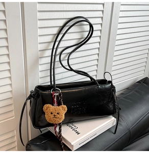 Close-up of black leather underarm bag with embossed text and a cute bear charm