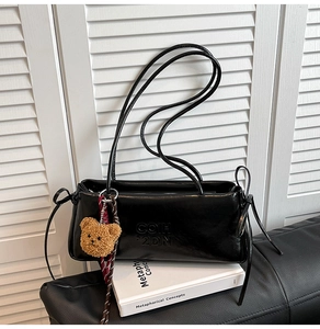 Detail of black soft leather underarm bag with glossy finish and cute plush bear charm