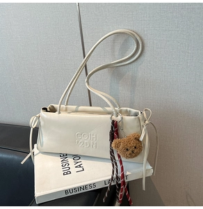 Detail of off-white leather underarm bag with teddy bear pendant on white books