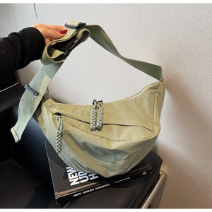 Close-up of light green nylon crescent bag featuring a woven zipper and wide shoulder strap
