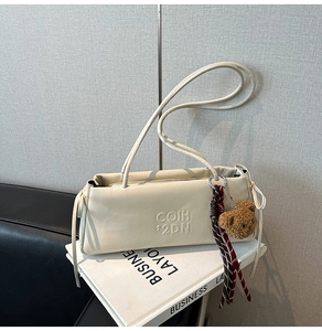 Detail of cream leather shoulder bag featuring embossed letters and a cute plush bear charm