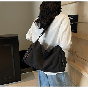 Detail of a black large capacity canvas shoulder bag with functional zippers and strap