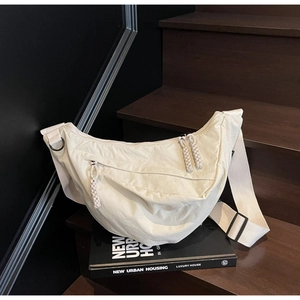 Close-up of a cream nylon dumpling bag featuring woven zipper pulls and wide strap