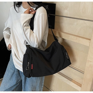 Model wearing a large black nylon crossbody bag with side zipper and red detail tag