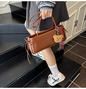 Detail of caramel brown leather baguette bag with letter embossing and cute bear charm