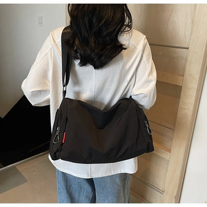 Detail of a black large-capacity crossbody bag showing its durable nylon fabric and red tag