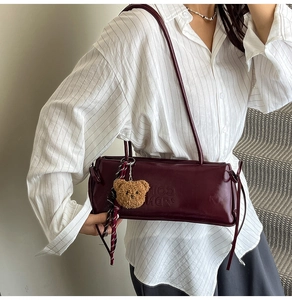 Detail of burgundy soft leather underarm bag with embossed text and plush bear charm
