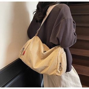 Detail of a large beige nylon shoulder bag showing durable wide straps and side pockets