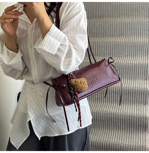 Detail of burgundy leather shoulder bag with side bow detail and teddy bear charm
