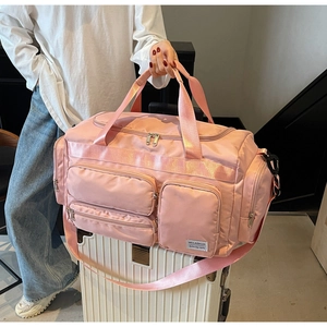 Borsa da viaggio in nylon rosa impermeabile con multitasche posata su una valigia bianca