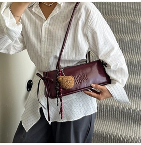 Detail of burgundy leather baguette bag with embossed letters and a brown bear pendant