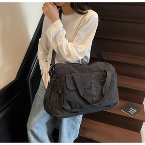 Black large capacity travel bag worn crossbody by model on stairs showing functional pockets