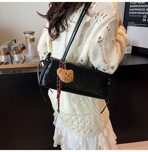 Detail of black faux leather shoulder bag with embossed letters and a cute bear charm