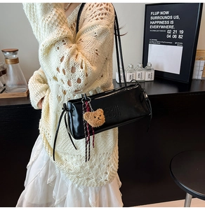 Detail of black faux leather underarm bag with embossed letters and brown plush bear charm