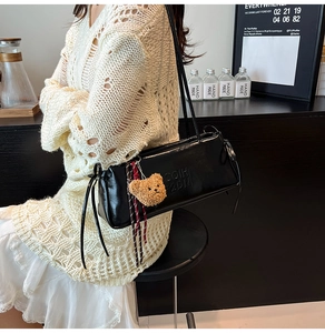 Detail of black faux leather baguette bag featuring a plush bear charm and embossed letters