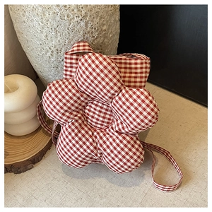 Détail du sac bandoulière en forme de fleur à carreaux rouges et blancs sur fond rustique