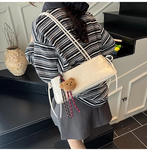 Detail of white patent leather baguette bag with embossed letters and plush bear charm