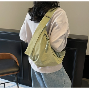 Detail of green crescent canvas crossbody bag featuring a woven zipper pull and wide strap