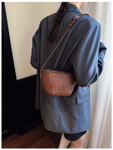 Detail of a brown woven bucket bag with smooth leather texture and adjustable strap